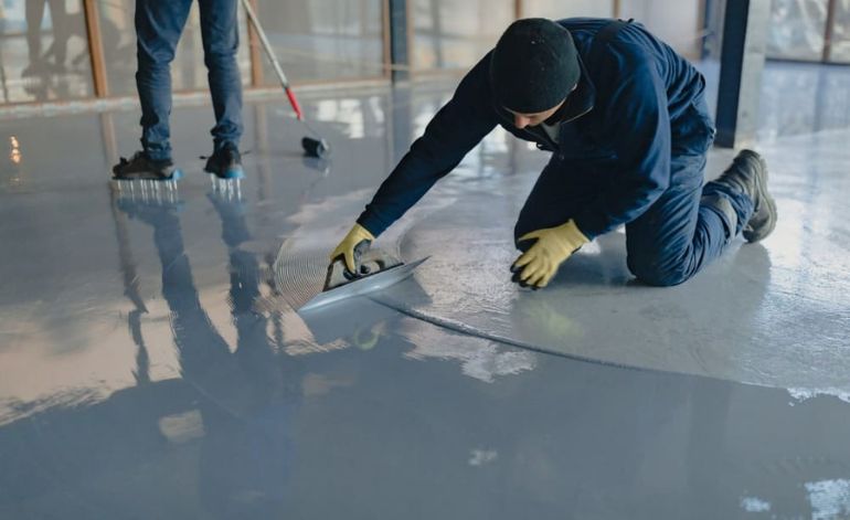 Two men engaged in epoxy flooring installation on a concrete surface in Miami, Florida.
