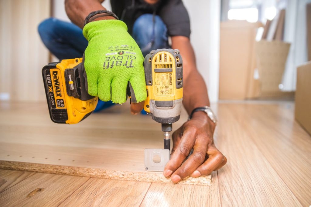 A man is using a drill to attach a wooden board, demonstrating skilled craftsmanship in woodworking.