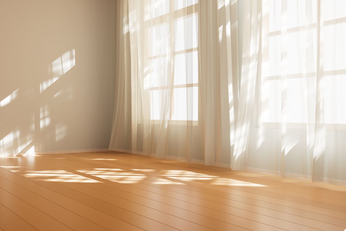 A bright, empty room illuminated by sunlight streaming through a large window, creating a warm and inviting atmosphere.