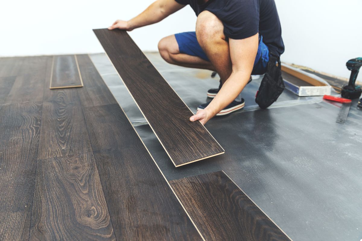 A man carefully installs wood flooring in a well-lit room, showcasing his craftsmanship and attention to detail.