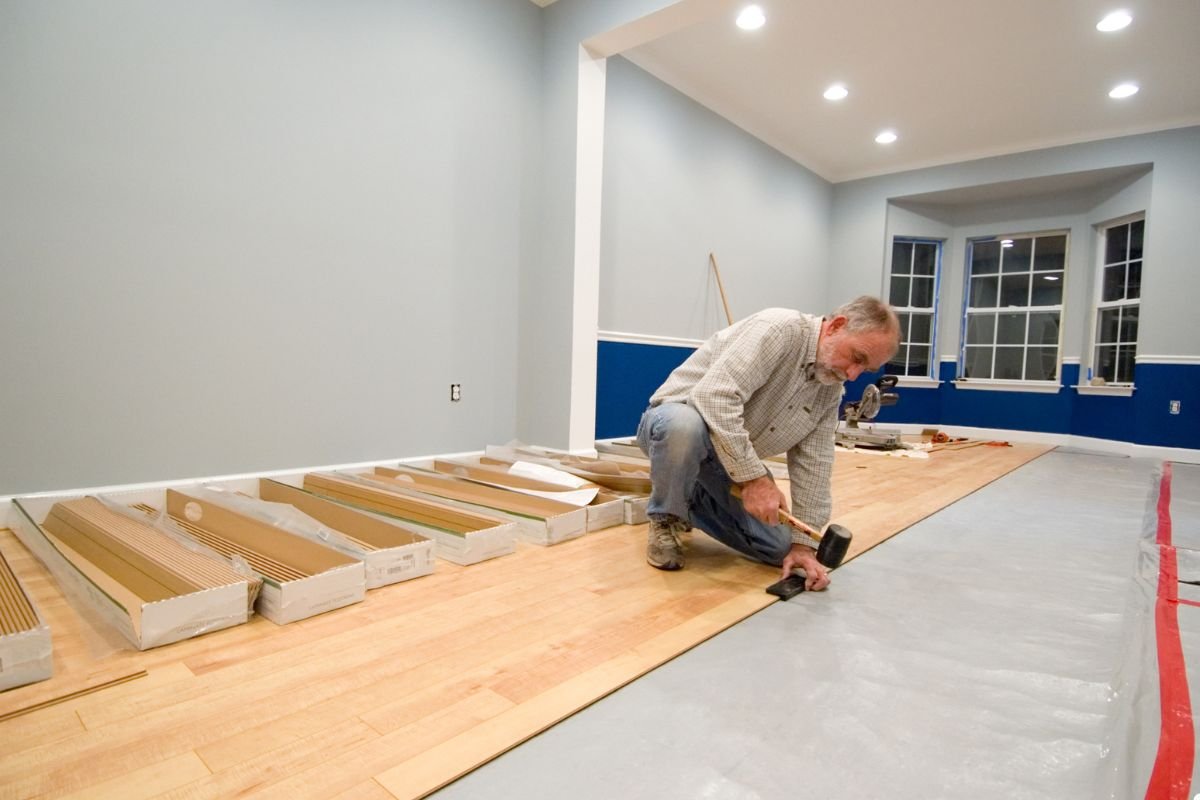 A man carefully installs hardwood flooring in a well-lit room, showcasing his craftsmanship and attention to detail.