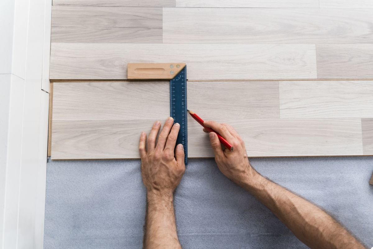 A man carefully lays down wood flooring, using a ruler to ensure precise measurements and alignment. 